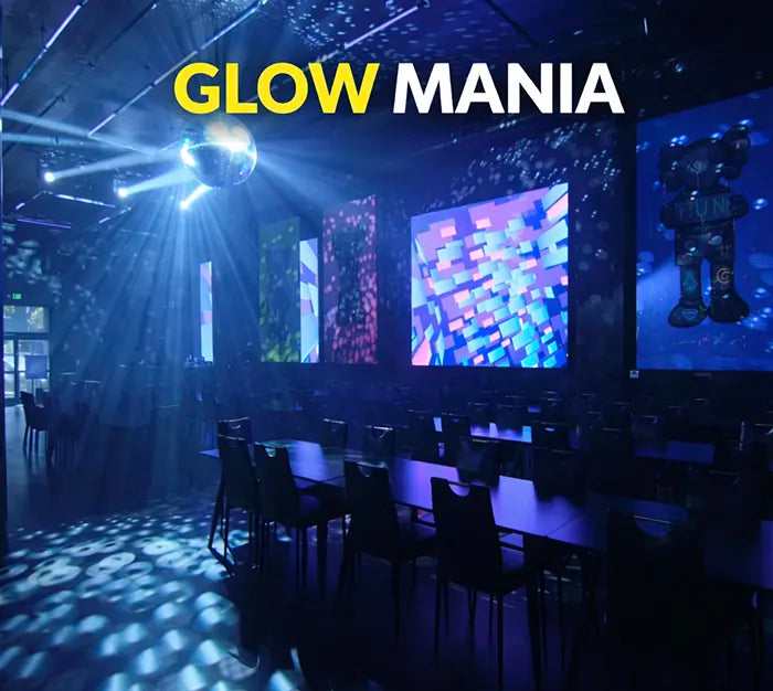 A dark event space features glowing blue and purple lights, a spinning disco ball, empty tables and chairs, and colorful digital screens. The words "GLOW MANIA" are displayed in bold yellow and white text at the top.