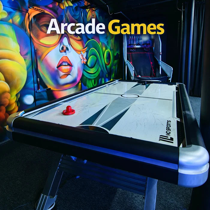 A modern air hockey table is in the foreground of a vibrant arcade room with colorful wall art featuring a stylized face, and the text “Arcade Games” appears above.