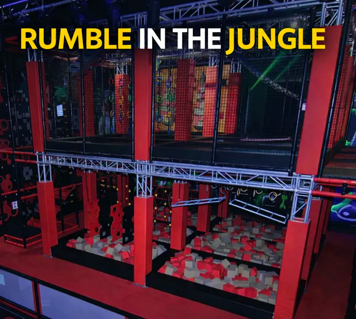 An indoor adventure park features a jungle-themed obstacle course above foam pits, with the words "RUMBLE IN THE JUNGLE" in bold yellow and white text at the top.