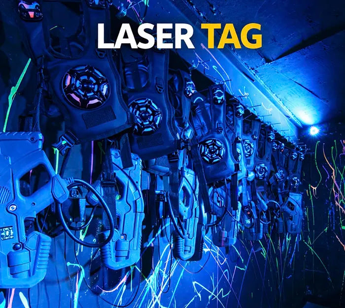 A row of laser tag vests and phasers hangs on a wall, illuminated by blue and black lights with neon paint splatters. The words "LASER TAG" appear at the top of the image.