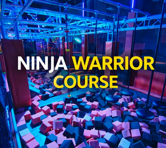 A brightly lit indoor ninja warrior course with obstacles and swinging ropes above a pit filled with multicolored foam blocks. The words “NINJA WARRIOR COURSE” are overlaid in bold white and yellow text.